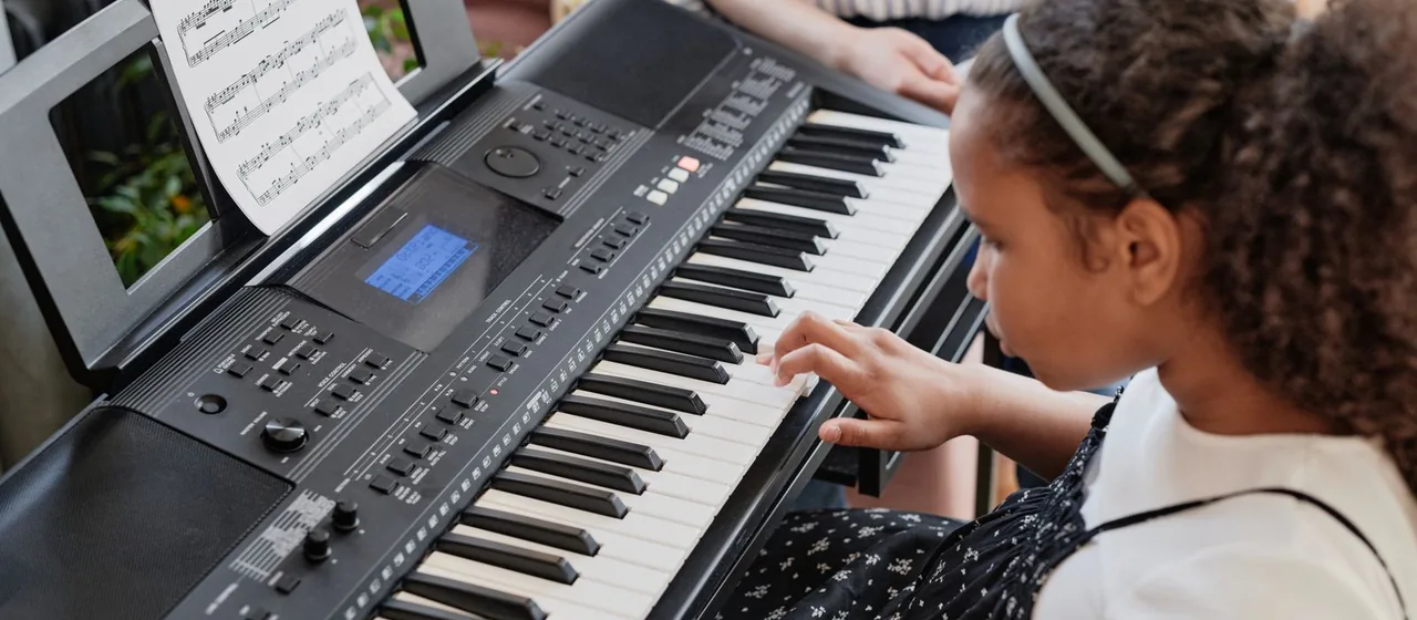 Criança concentrada tocando teclado em casa, com a partitura ao lado