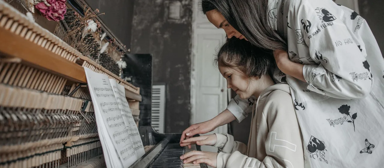 Mãe acompanhando a filha tocando piano em casa